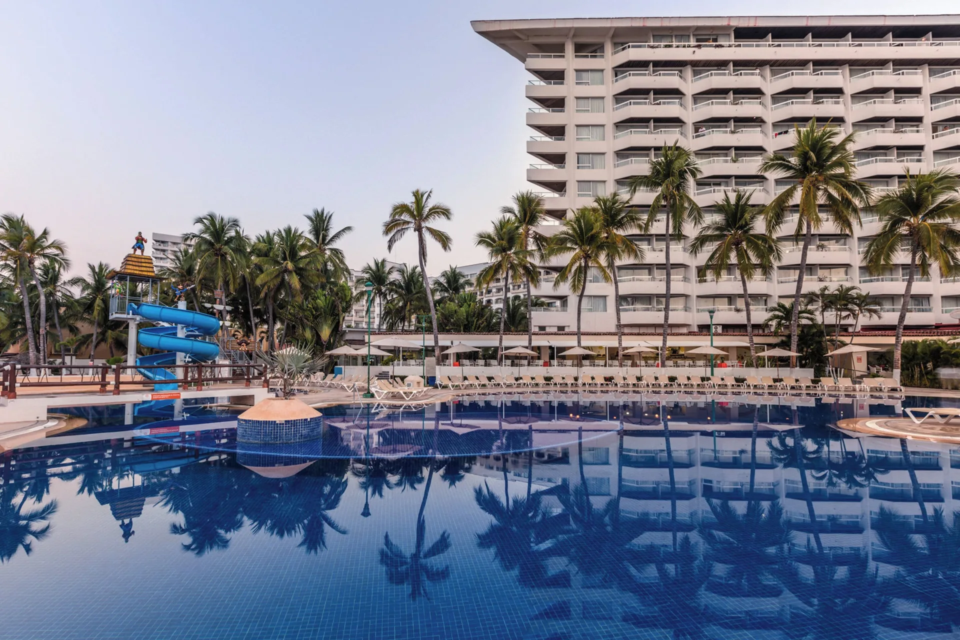 Main pool with waterslide, palms, loungers, and hotel tower at Krystal Ixtapa.