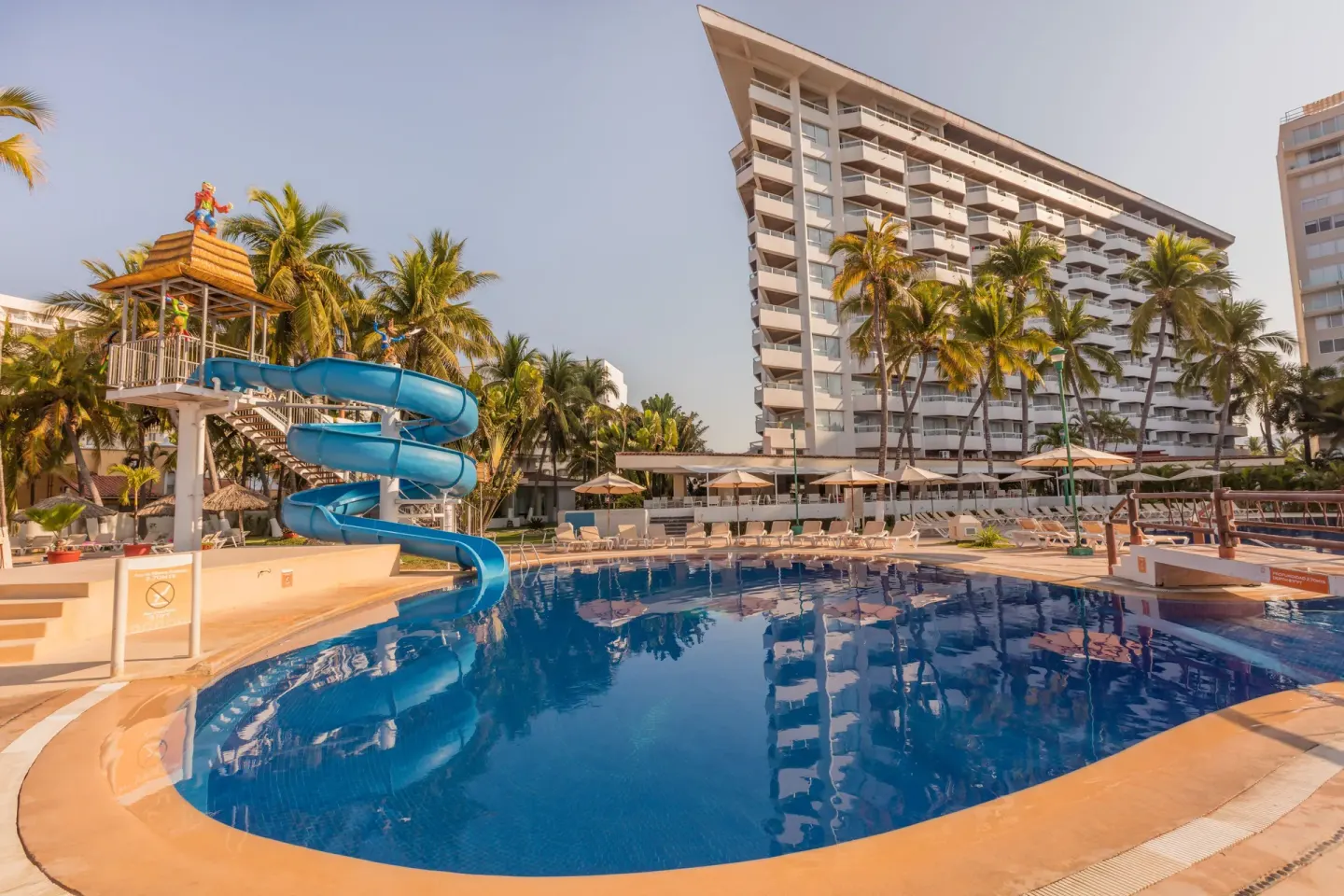 A large pool with a blue waterslide sits in front of Krystal Ixtapa.
