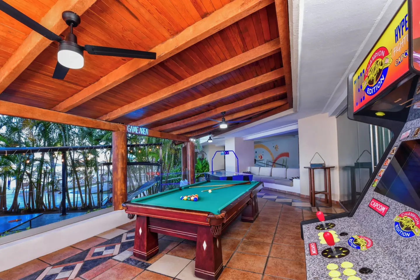 A game area with a pool table and arcade cabinet overlooks palms at Krystal Ixtapa.