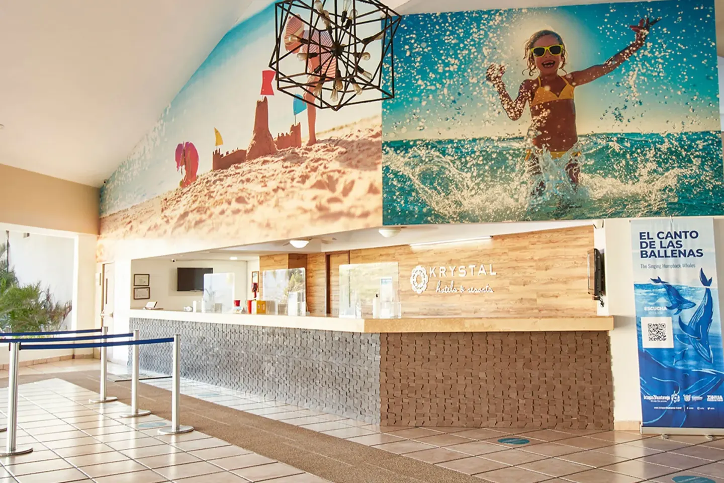 Reception desk below beach murals and a whale poster at Krystal Ixtapa.