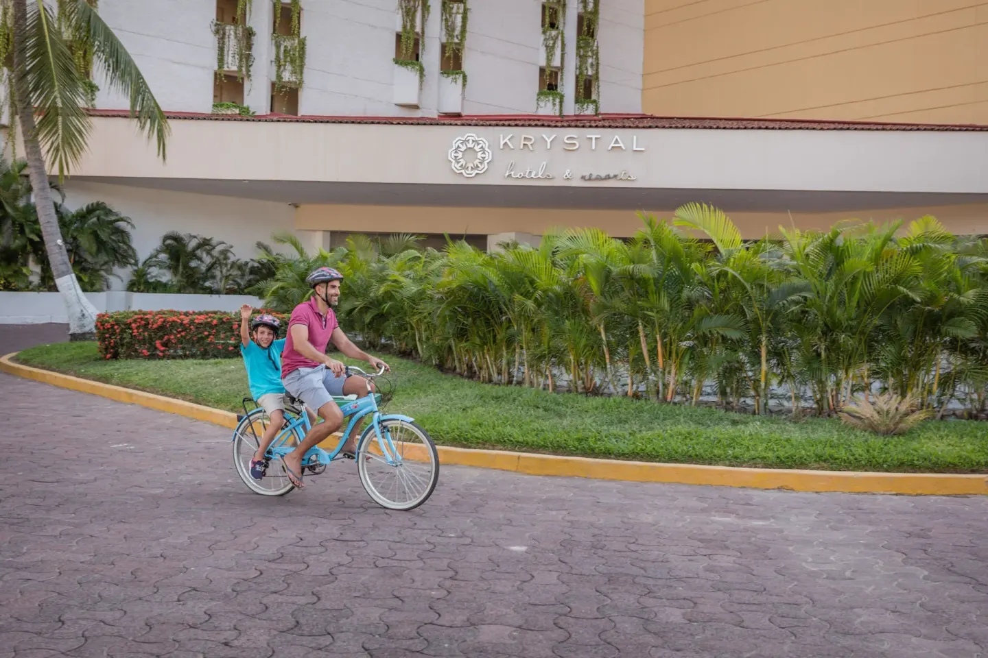 Guests ride a bicycle past the signed entrance facade at Krystal Ixtapa.