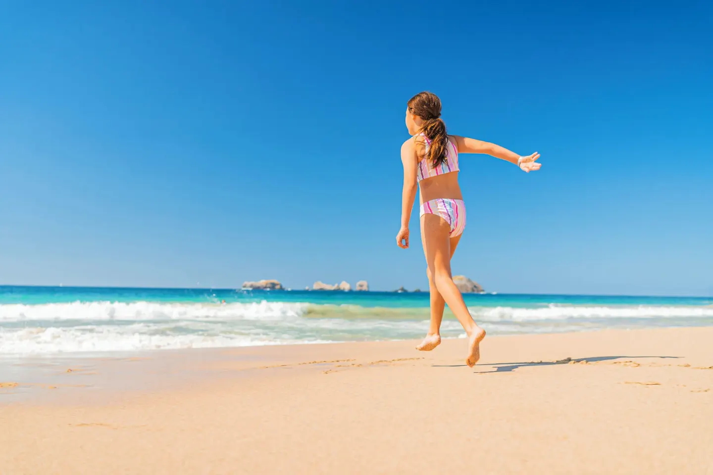 Child jumping on the sandy beach with ocean waves at Krystal Ixtapa.