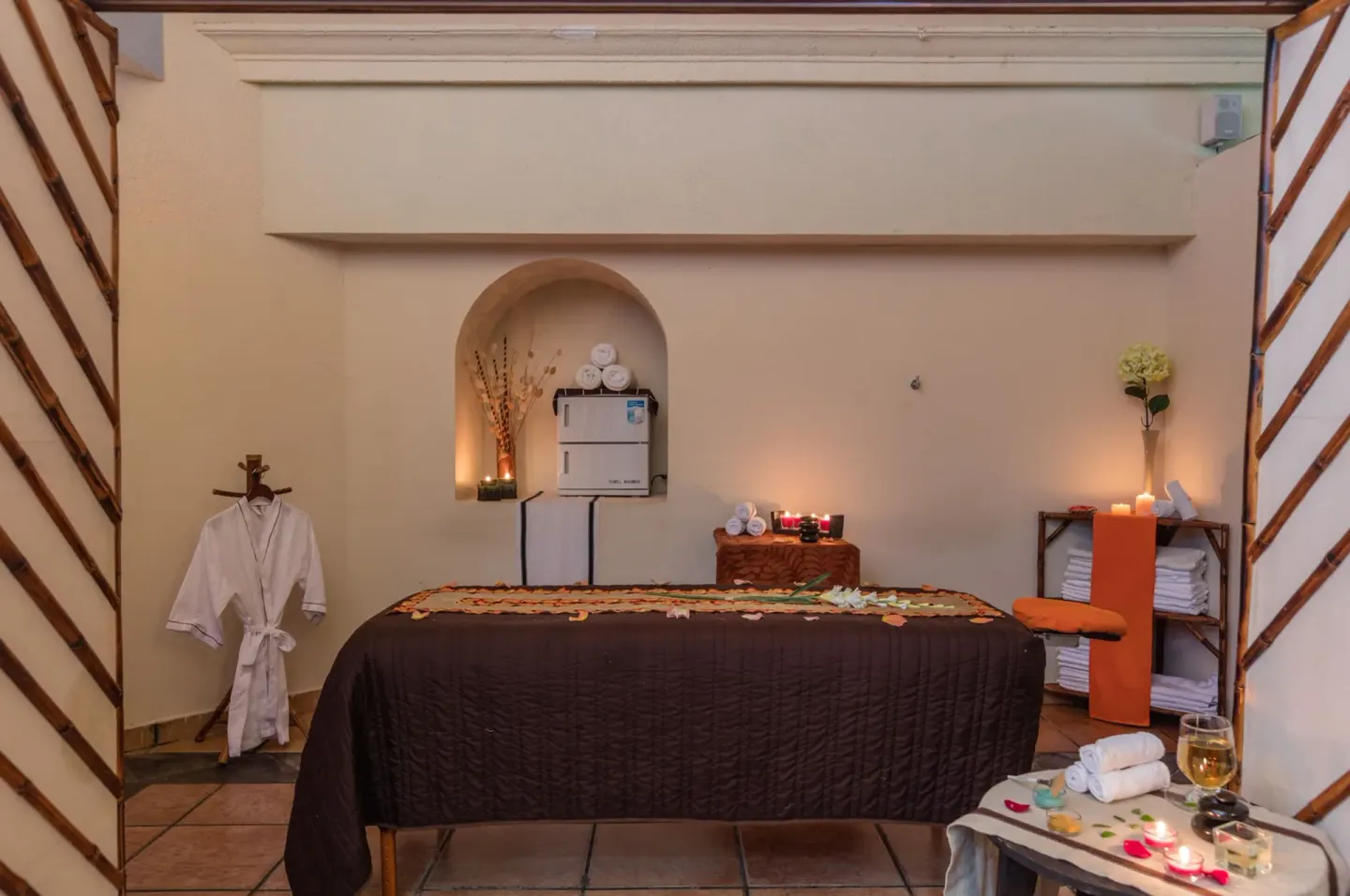 Spa treatment room with massage table, robe, towels, candles, and flower decor at Krystal Ixtapa.