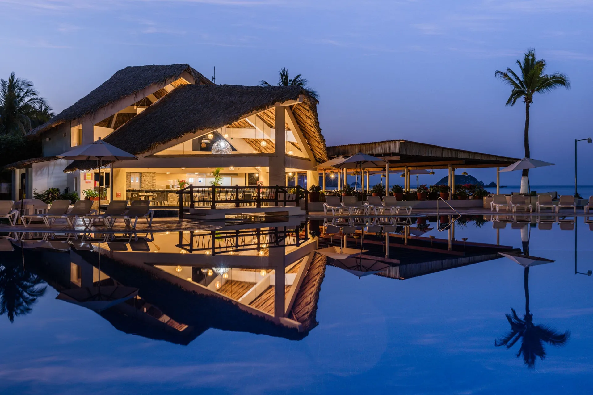 Thatched poolside restaurant building reflected in the pool at dusk at Krystal Ixtapa.