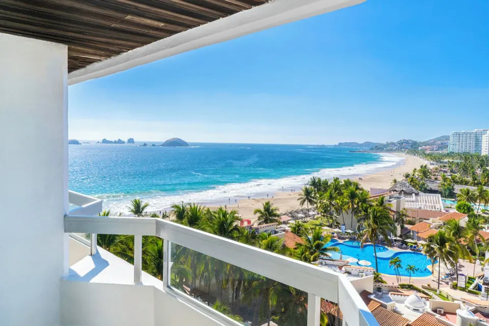 Ocean View room balcony with coastline, ocean, pools, and palms at Krystal Ixtapa.