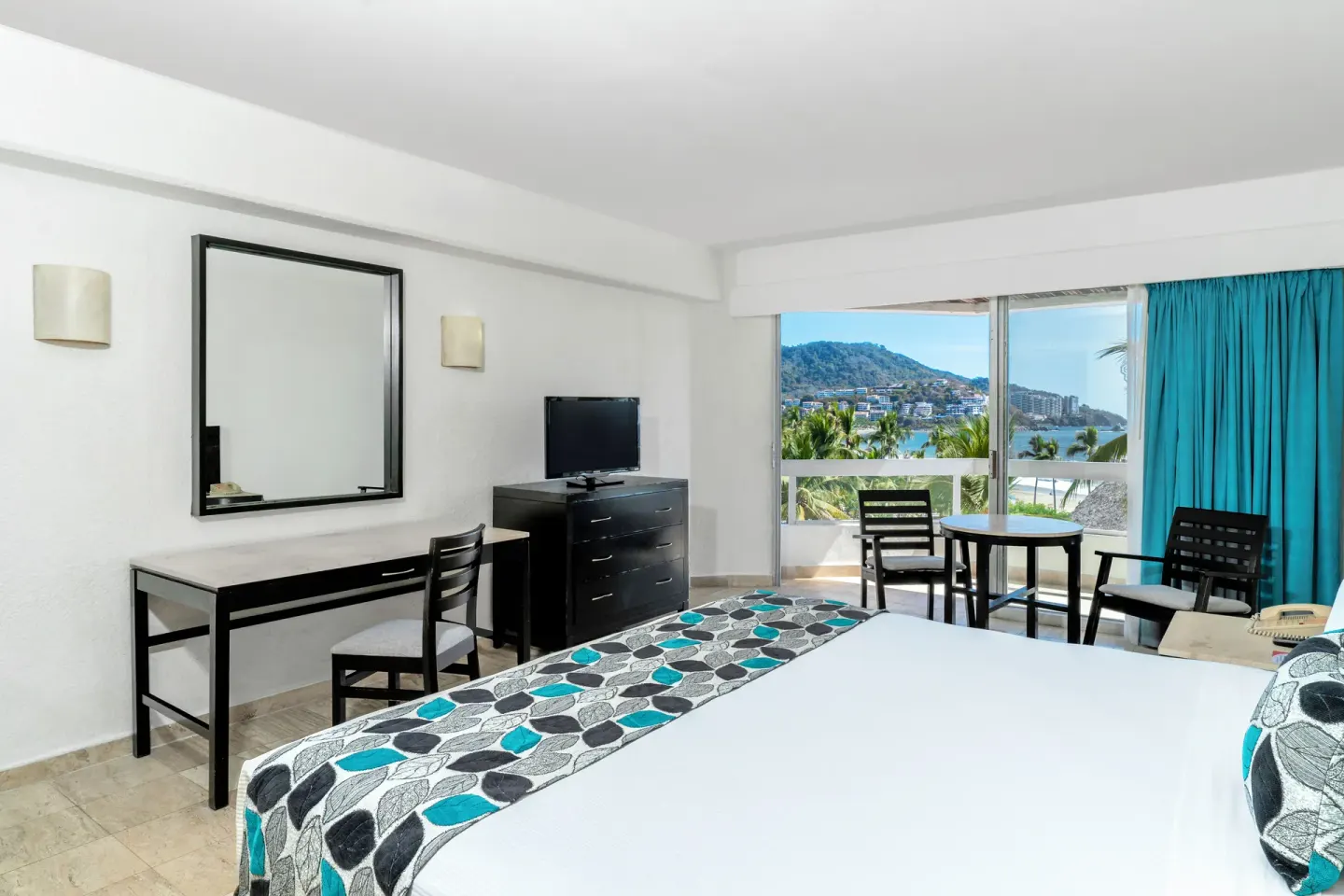 Ocean View room with bed, desk, TV, and balcony facing the bay at Krystal Ixtapa.