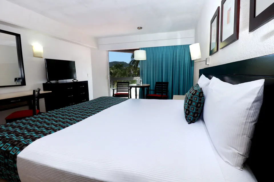 Standard room king bed with dresser, TV and balcony view at Krystal Ixtapa.