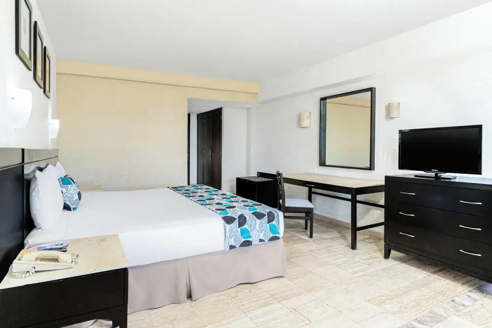 Standard Room Garden View king bed with desk, mirror and TV at Krystal Ixtapa.