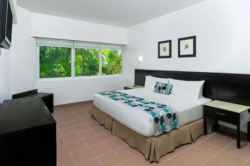 Standard Room Garden View king bed beside wide garden windows at Krystal Ixtapa.