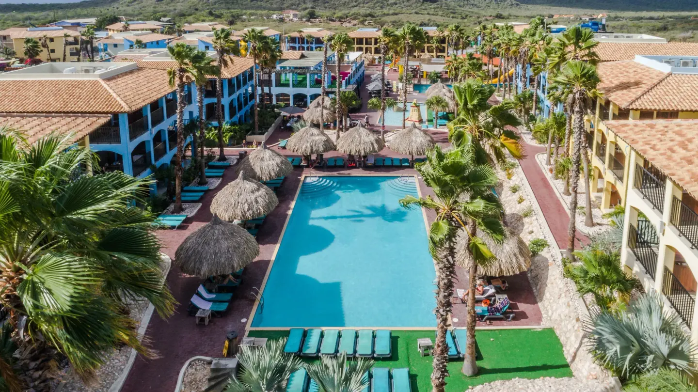 Aerial view of the main pool, palms, and resort buildings at Kunuku Resort Curacao.