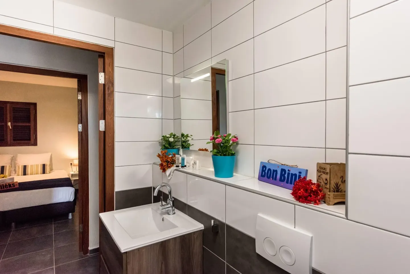 Tiled bathroom vanity with mirror and doorway to a bedroom at Kunuku Resort Curacao.