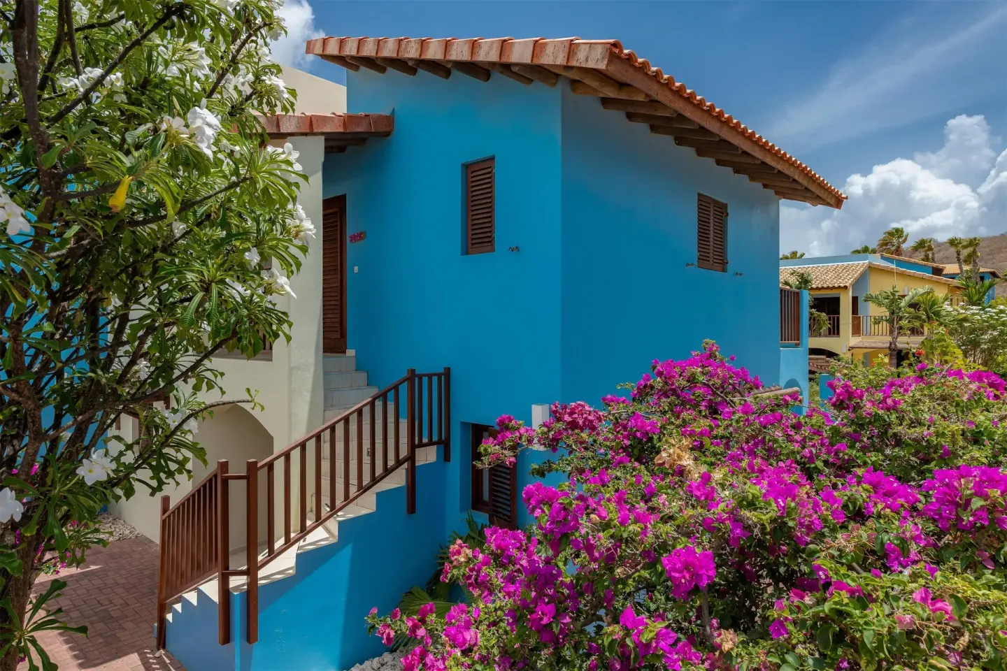 Blue resort building with stairs and flowering shrubs at Kunuku Resort Curacao.