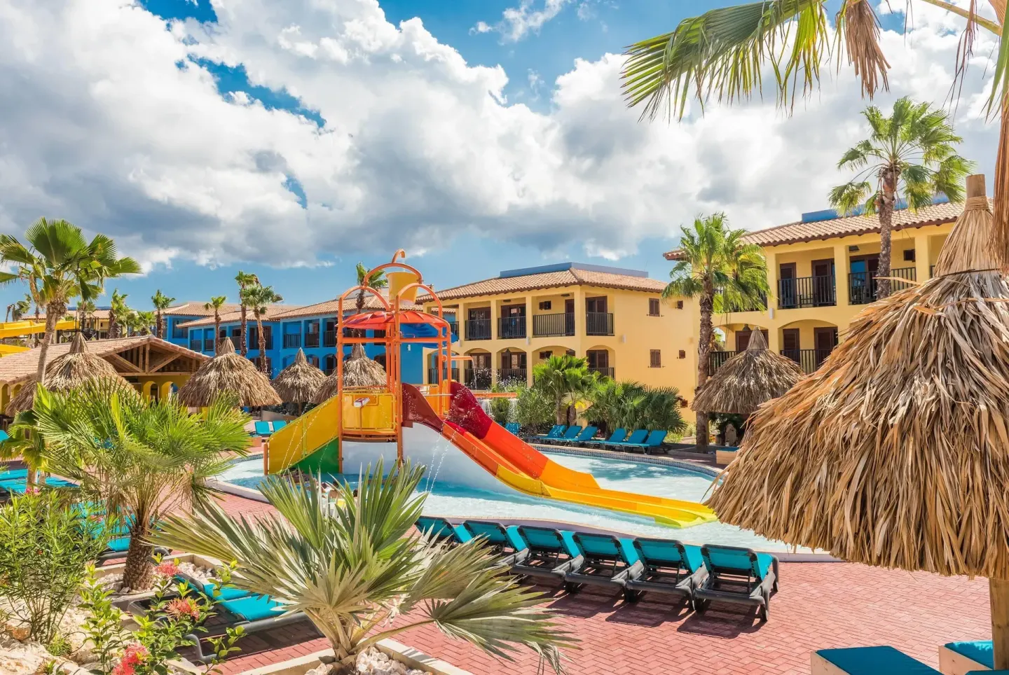 Colorful water slides, loungers, palms, and guest buildings at Kunuku Resort Curacao.