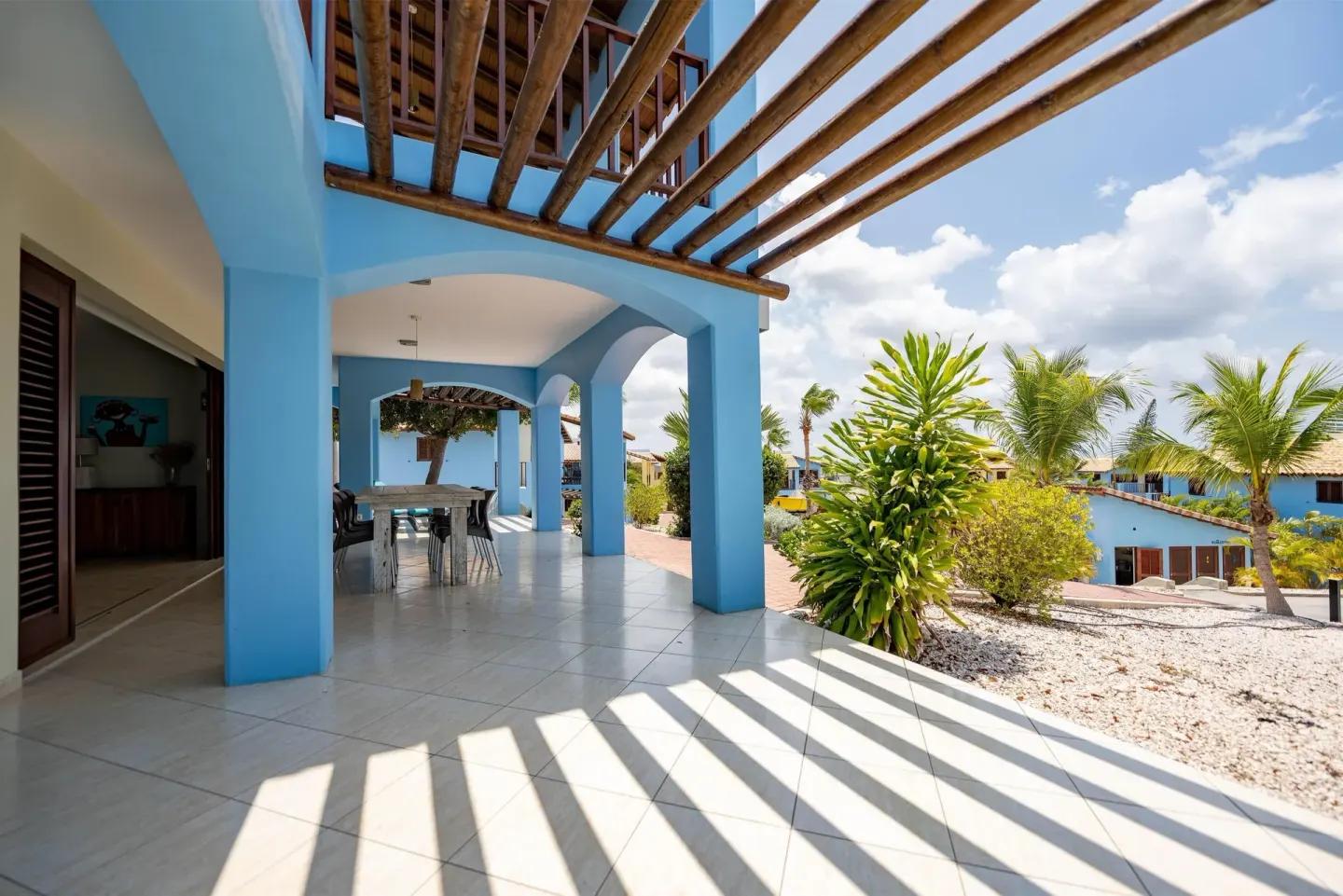 Covered blue terrace with dining table and palm landscaping at Kunuku Resort Curacao.
