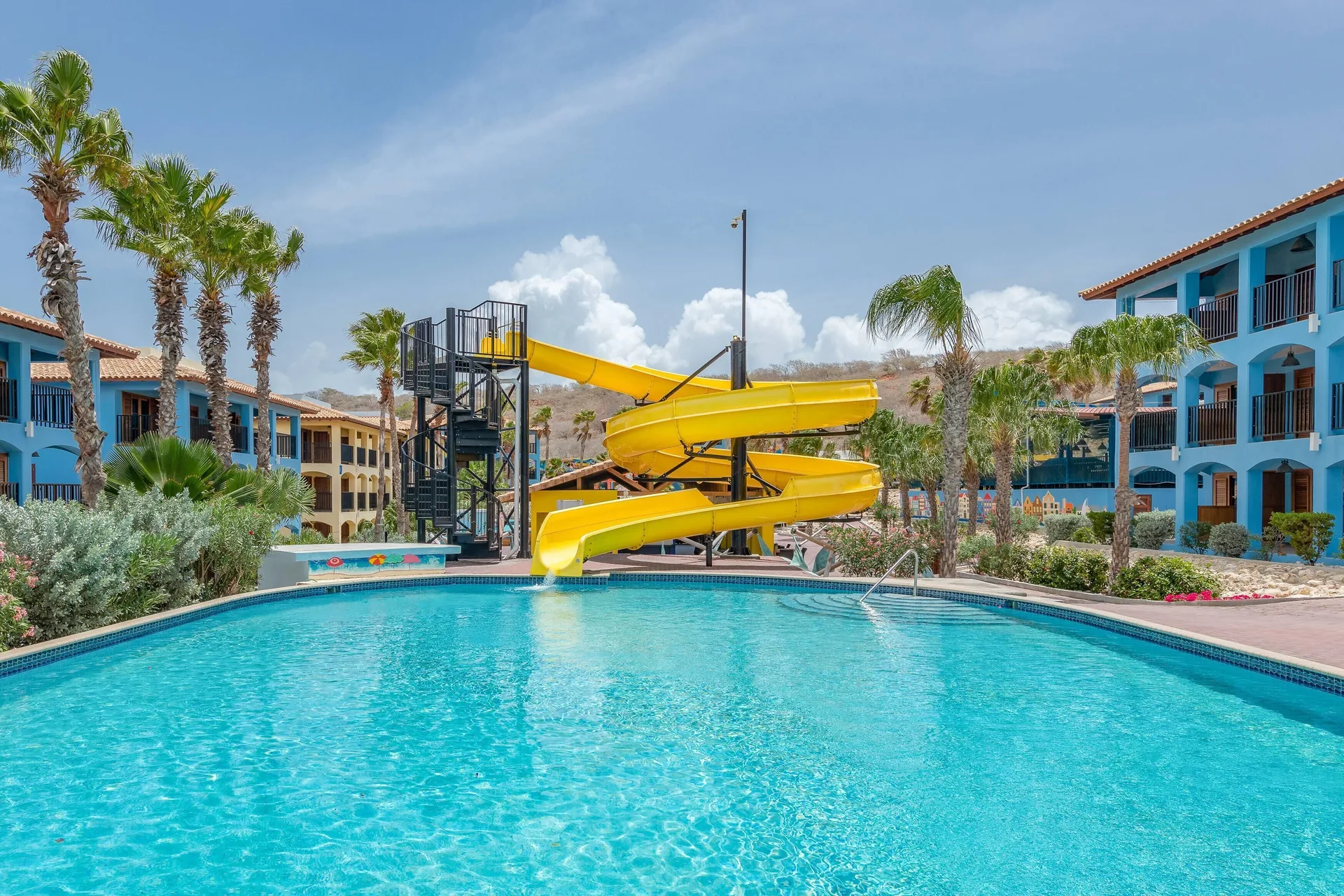 Large pool with a yellow spiral waterslide at Kunuku Resort Curacao.