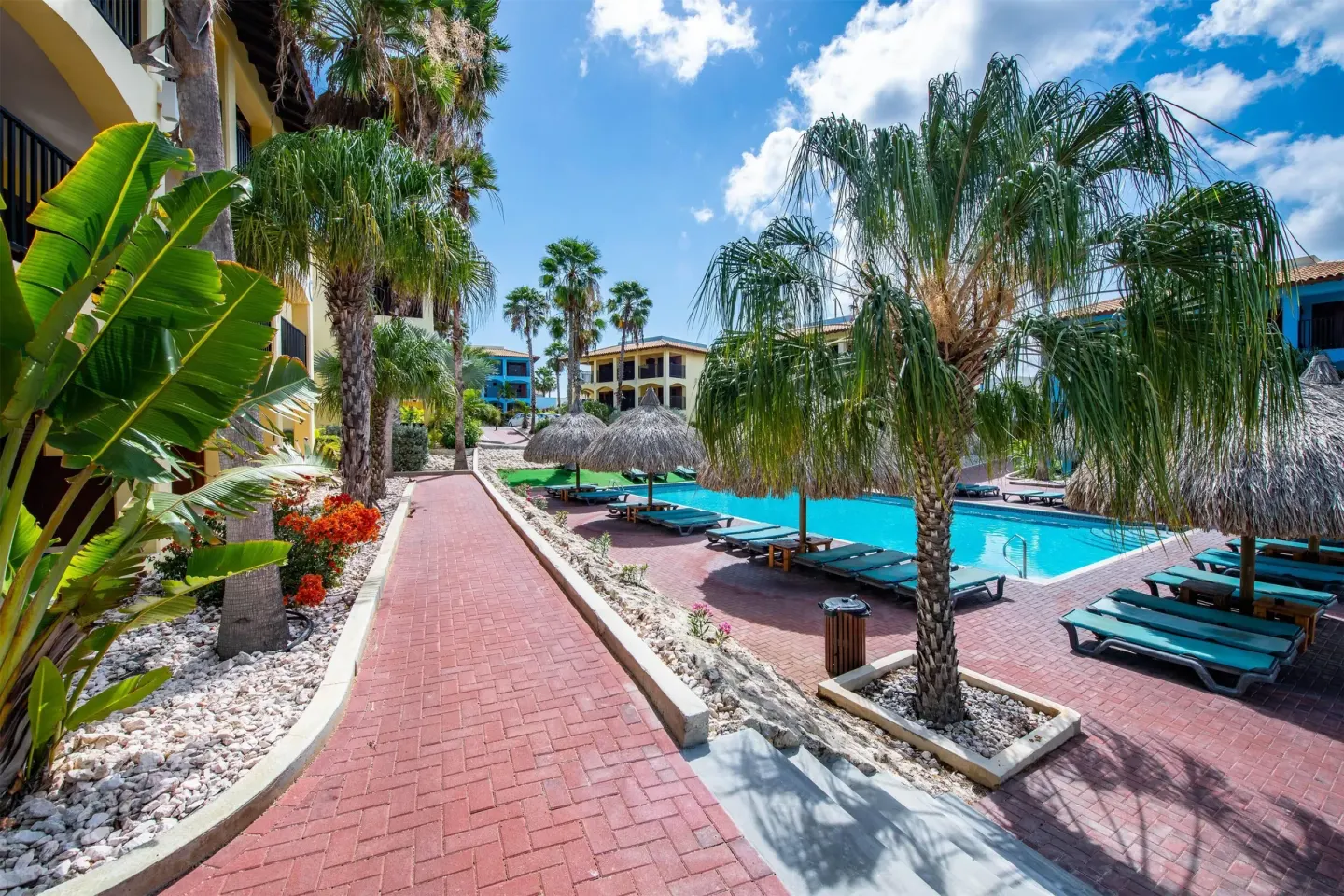 Brick walkway beside a pool with palms and loungers at Kunuku Resort Curacao.