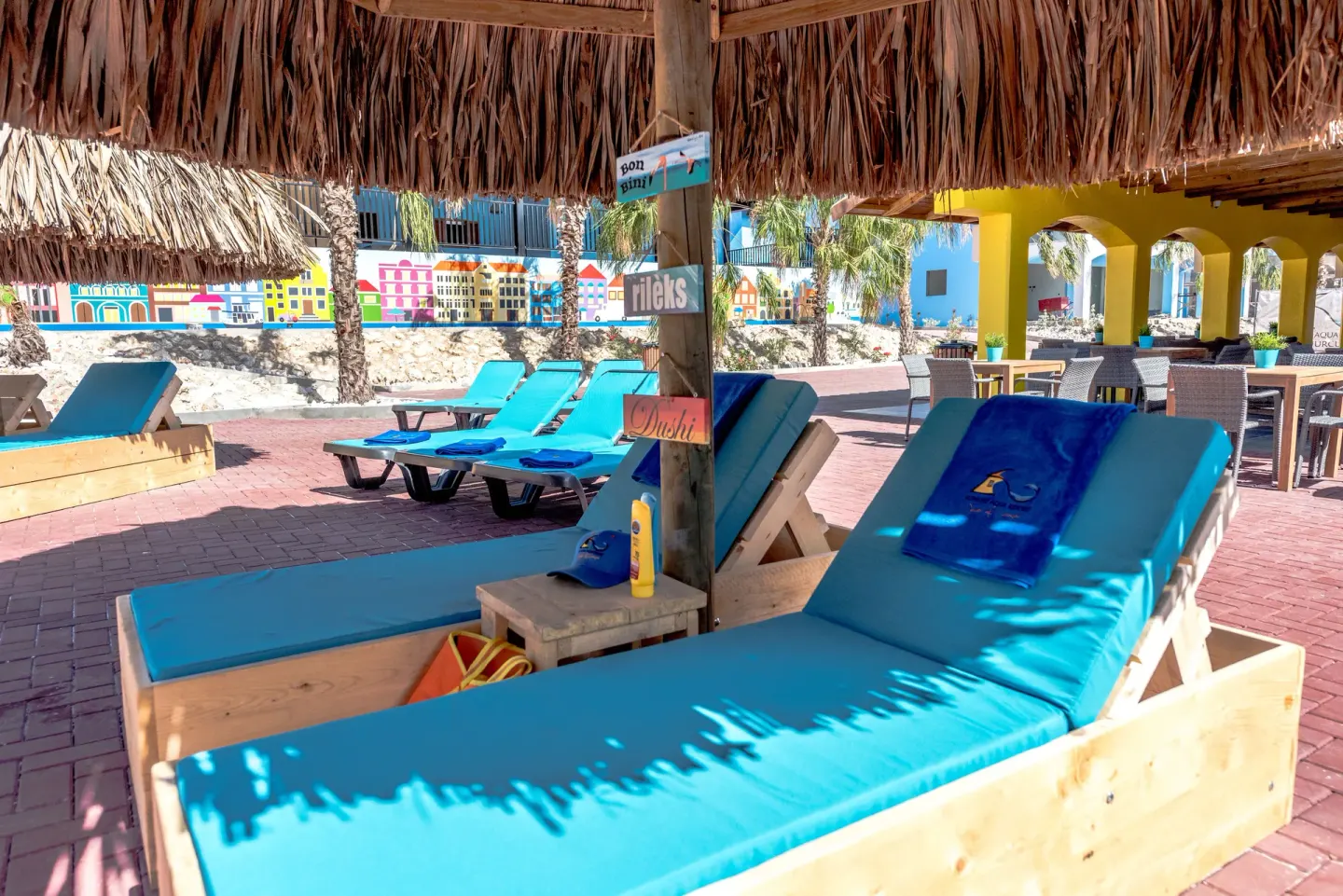 Thatched shade cabana with turquoise loungers near dining tables at Kunuku Resort Curacao.