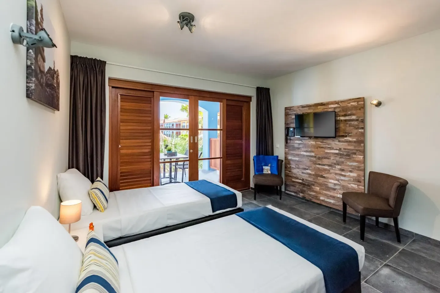 Twin-bed guest room with TV wall and balcony doors at Kunuku Resort Curacao.