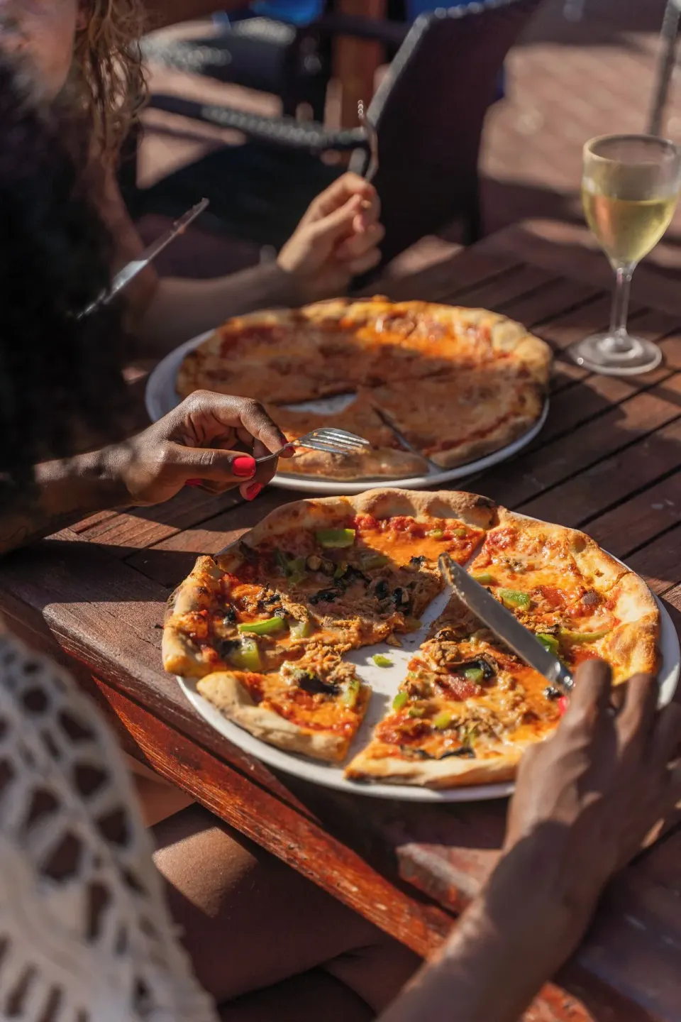 Guests share pizzas and a glass of wine at an outdoor table at Kunuku Resort Curacao.