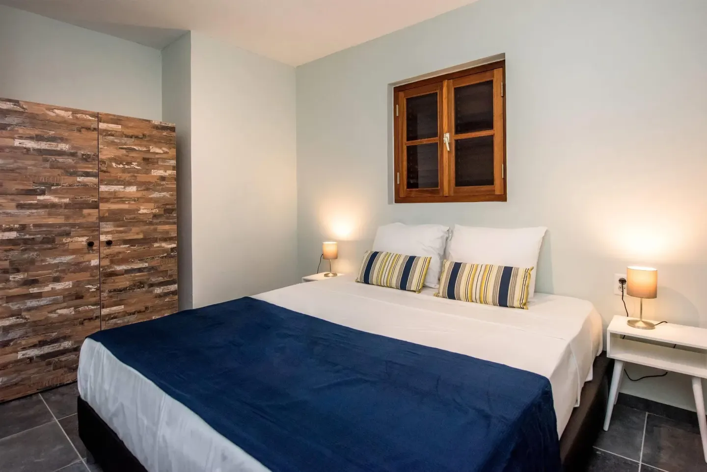 Bedroom with a double bed, blue throw, and wood wardrobe at Kunuku Resort Curacao.