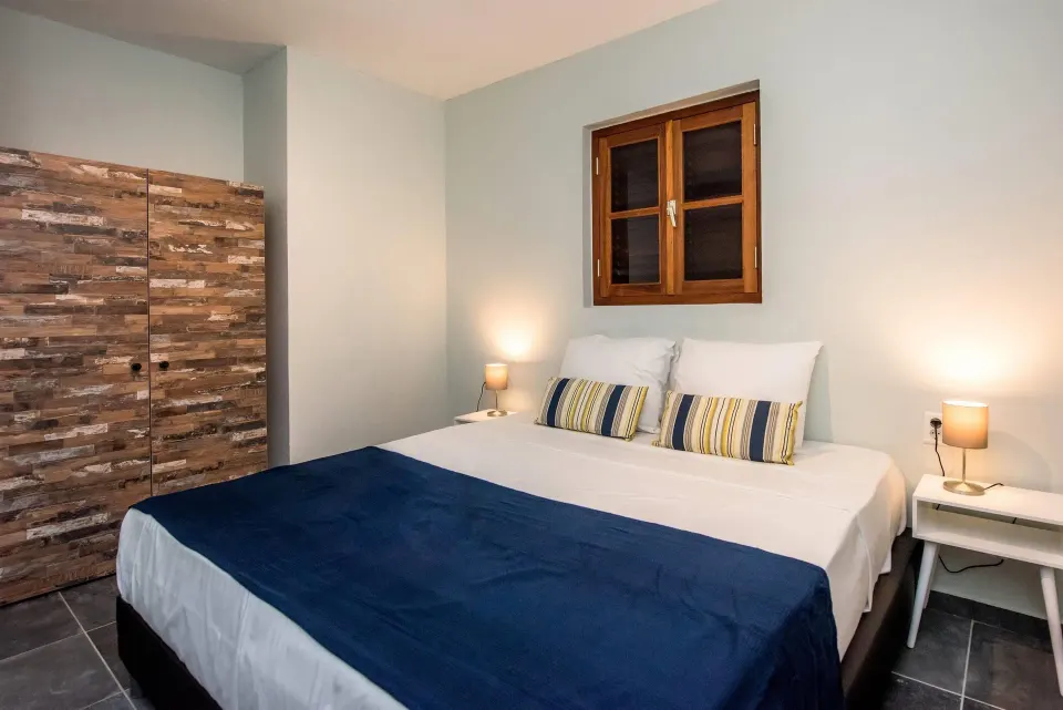 Bedroom with a double bed, blue throw, and wood wardrobe at Kunuku Resort Curacao.