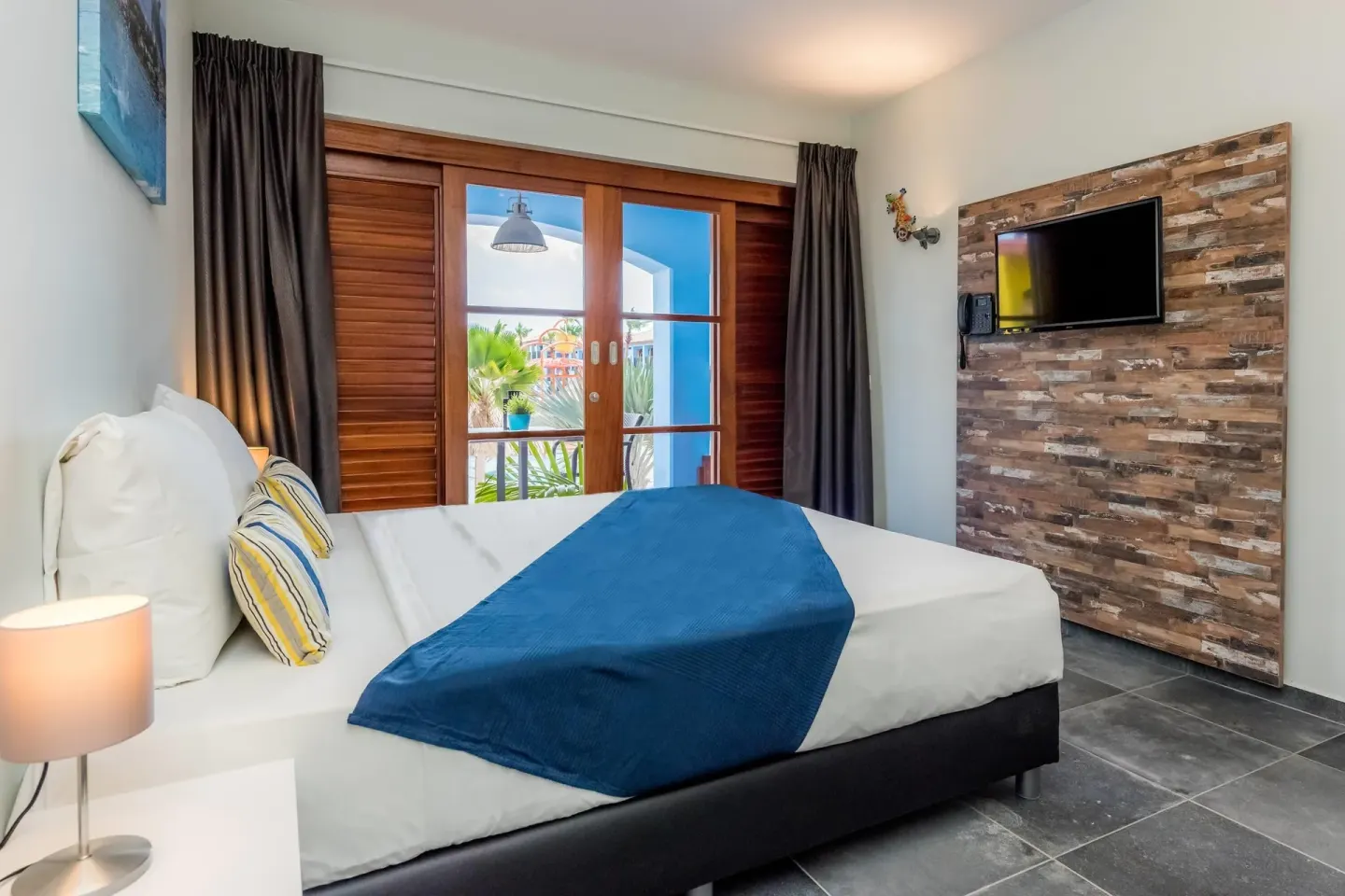 Standard Room bed, TV wall, and balcony doors at Kunuku Resort Curacao.