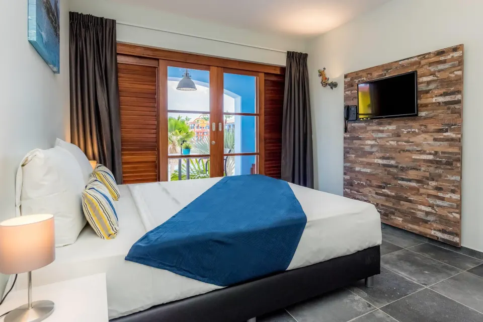 Standard Room bed, TV wall, and balcony doors at Kunuku Resort Curacao.