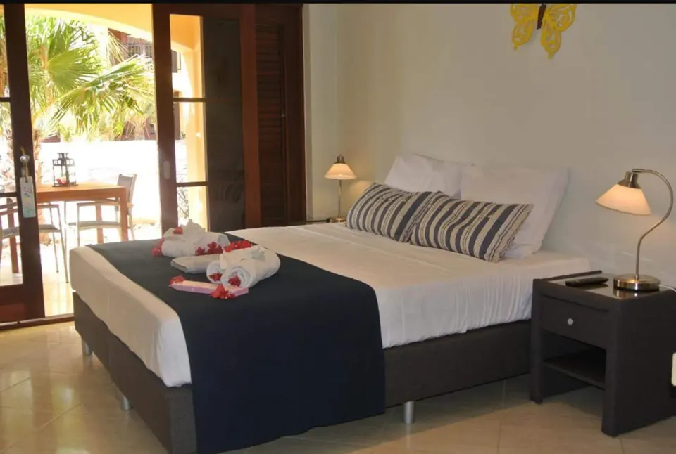 Standard Room bed with bedside lamps and terrace doors at Kunuku Resort Curacao.