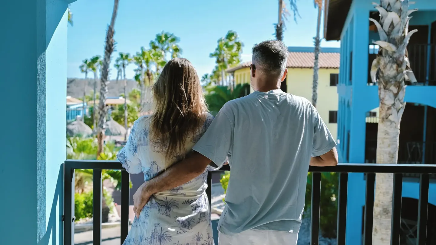 Couple standing on a suite balcony overlooking the grounds at Kunuku Resort Curacao.