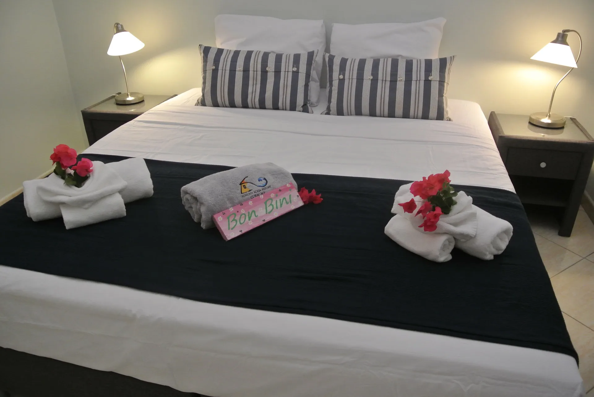 Suite bed with lamps, towels, flowers, and welcome sign at Kunuku Resort Curacao.