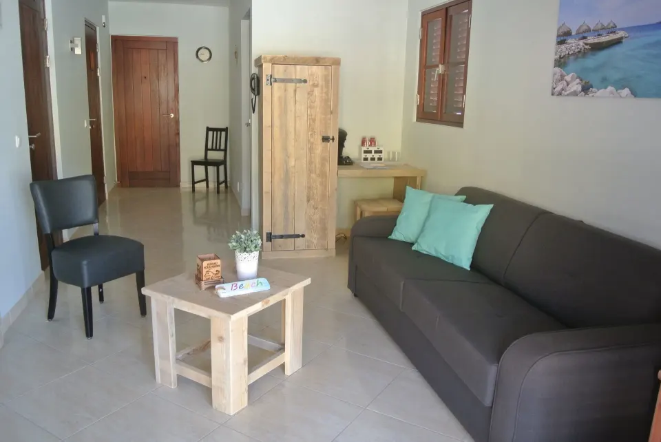 Suite living room with sofa, coffee table, chair, and wooden cabinet at Kunuku Resort Curacao.