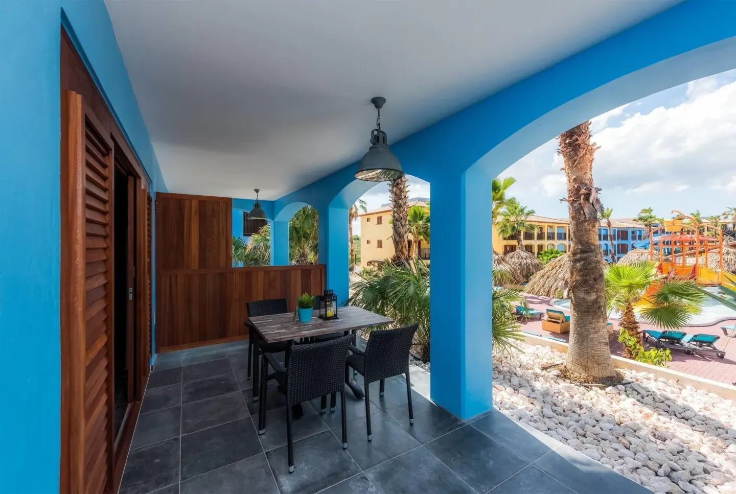 Suite terrace with table, chairs, blue arches, and pool area view at Kunuku Resort Curacao.