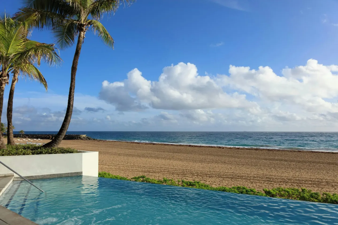 Pool edge, palm trees, sandy beach, and ocean at La Concha Resort, Puerto Rico.