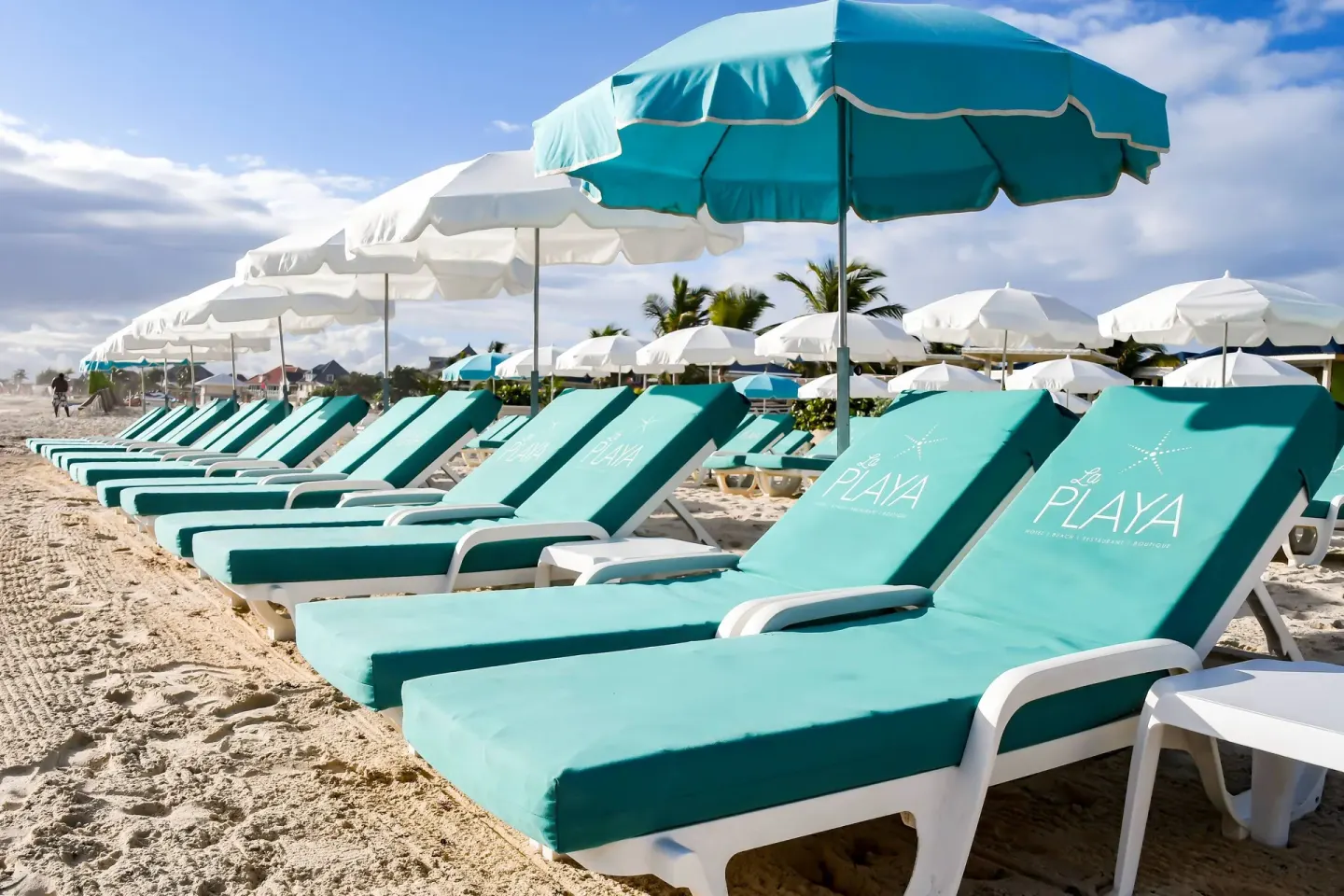 Angled row of turquoise beach loungers and umbrellas on the sand at La Playa Orient Bay.
