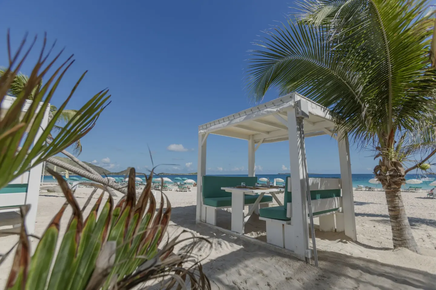 White beach cabana with turquoise seating and palms at La Playa Orient Bay.