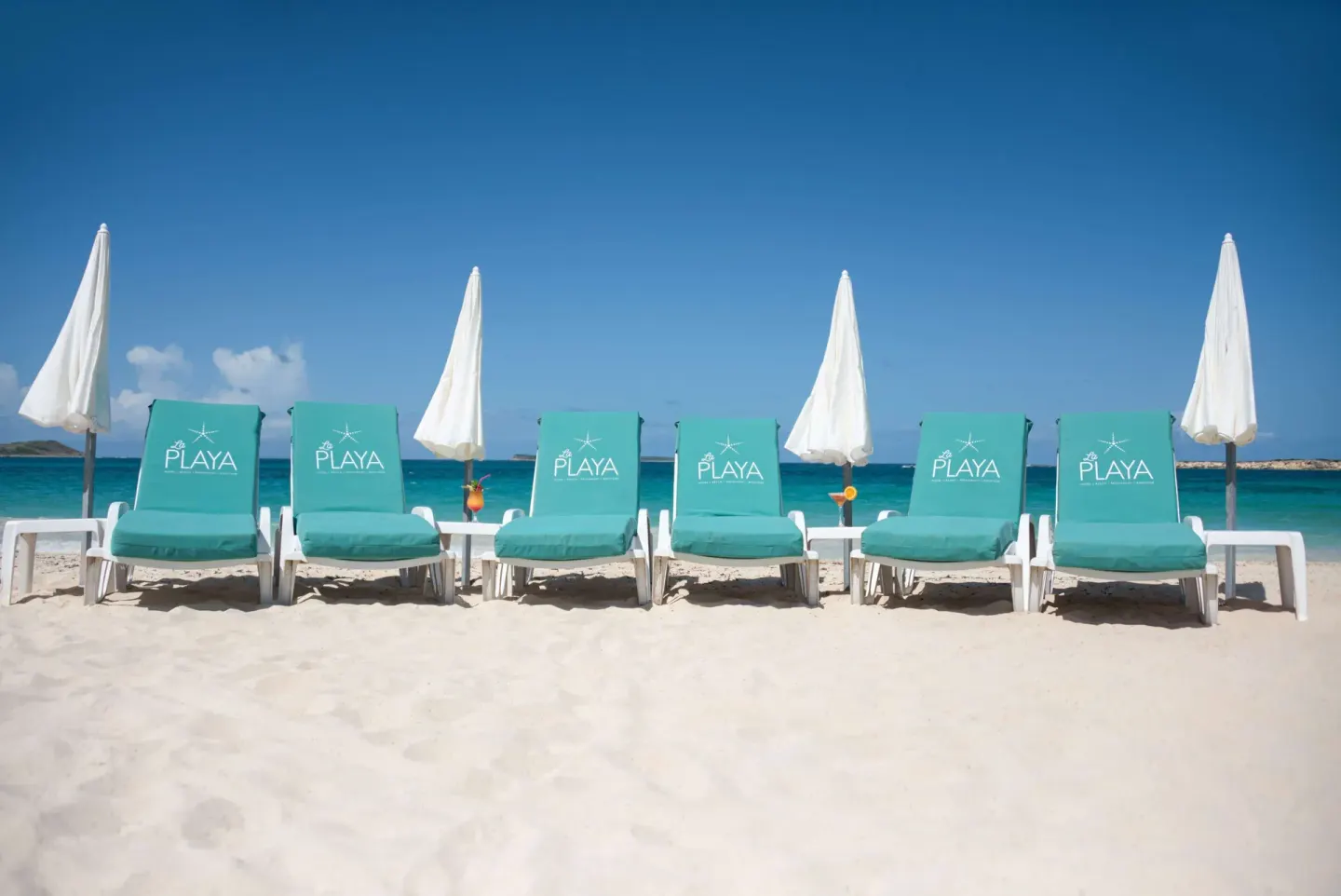 Turquoise beach loungers and white umbrellas facing the sea at La Playa Orient Bay.