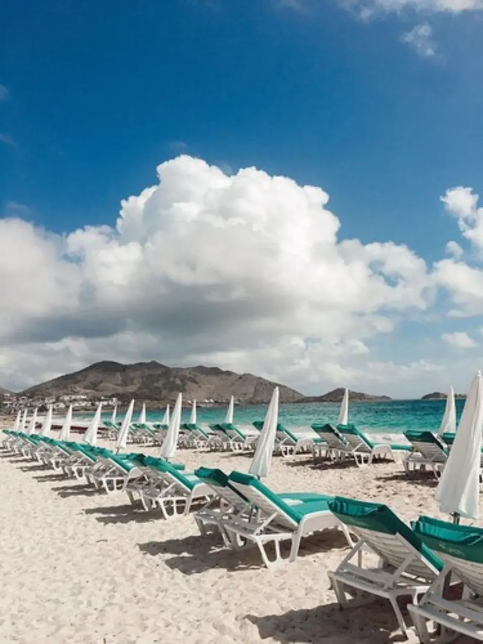 Rows of turquoise loungers and white umbrellas on the beach at La Playa Orient Bay.