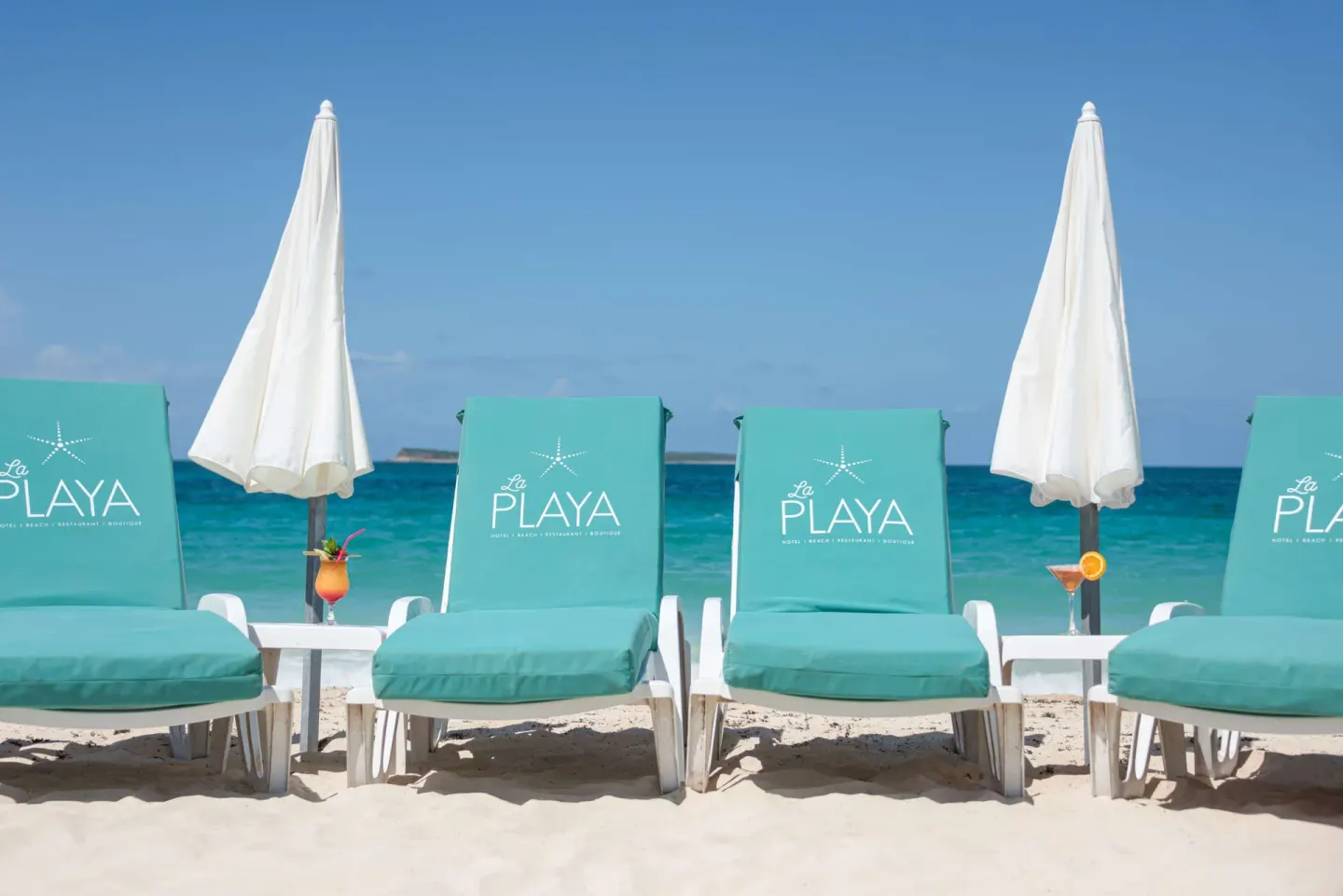 Close view of turquoise beach loungers, white umbrellas, and drinks at La Playa Orient Bay.