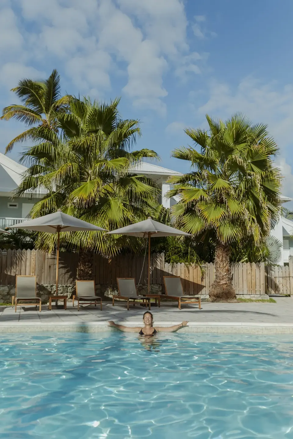 Guest standing in the pool with loungers, umbrellas and palms at La Playa Orient Bay.