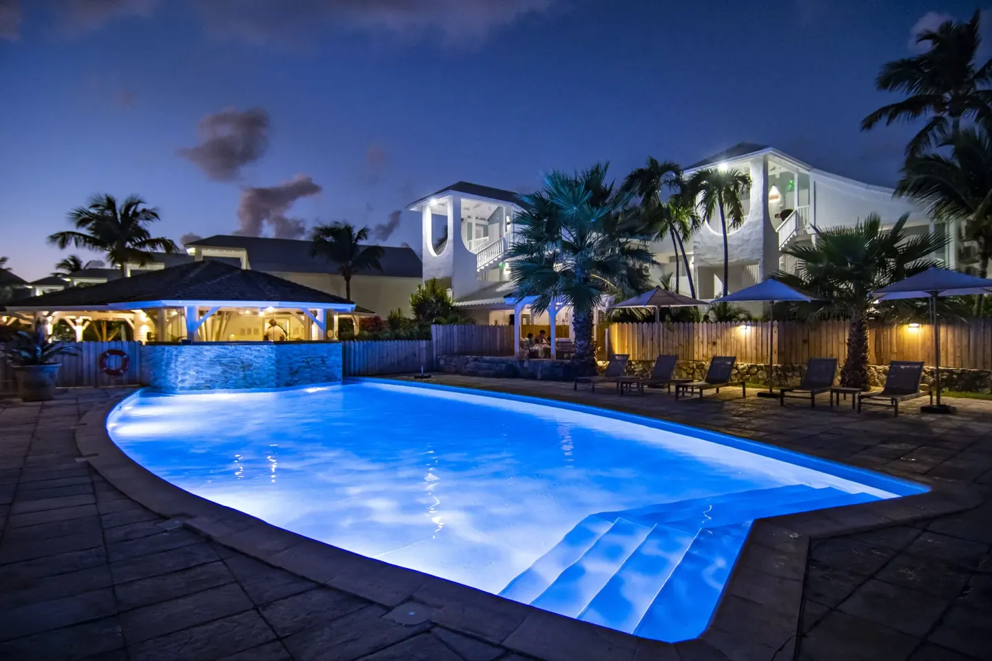 Evening pool glowing blue beside palm trees and resort buildings at La Playa Orient Bay.
