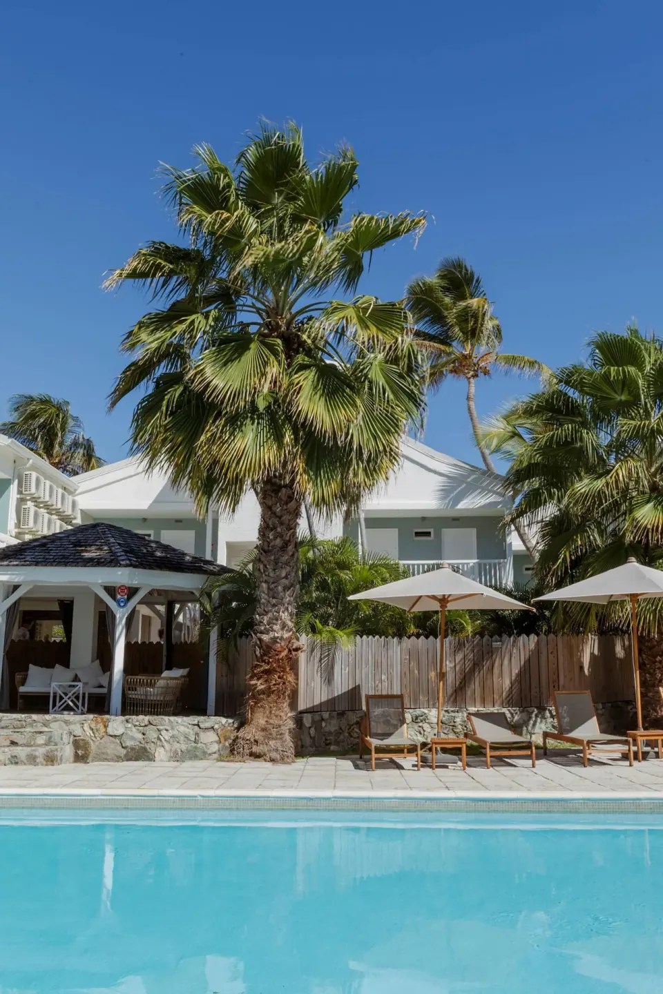 Pool edge with palms, loungers, umbrellas and white buildings at La Playa Orient Bay.
