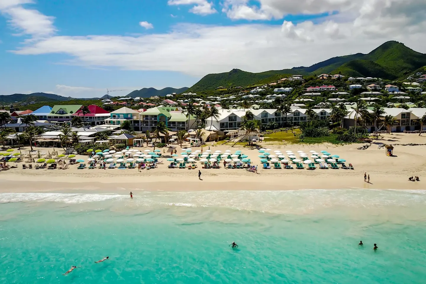 Wide aerial view of La Playa Orient Bay beach, turquoise water, and hillside buildings.