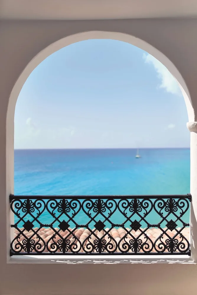 Arched balcony railing framing turquoise sea and a sailboat at La Samanna, St Martin.