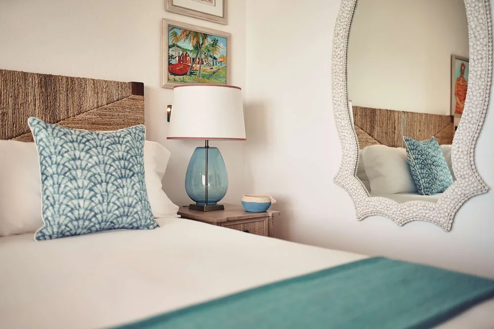 Guest room bed with woven headboard and shell-framed mirror at La Samanna, St Martin.