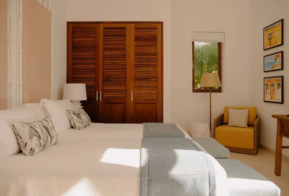 Bright guest room with bed, louvered wardrobe and yellow chair at La Samanna, St Martin.