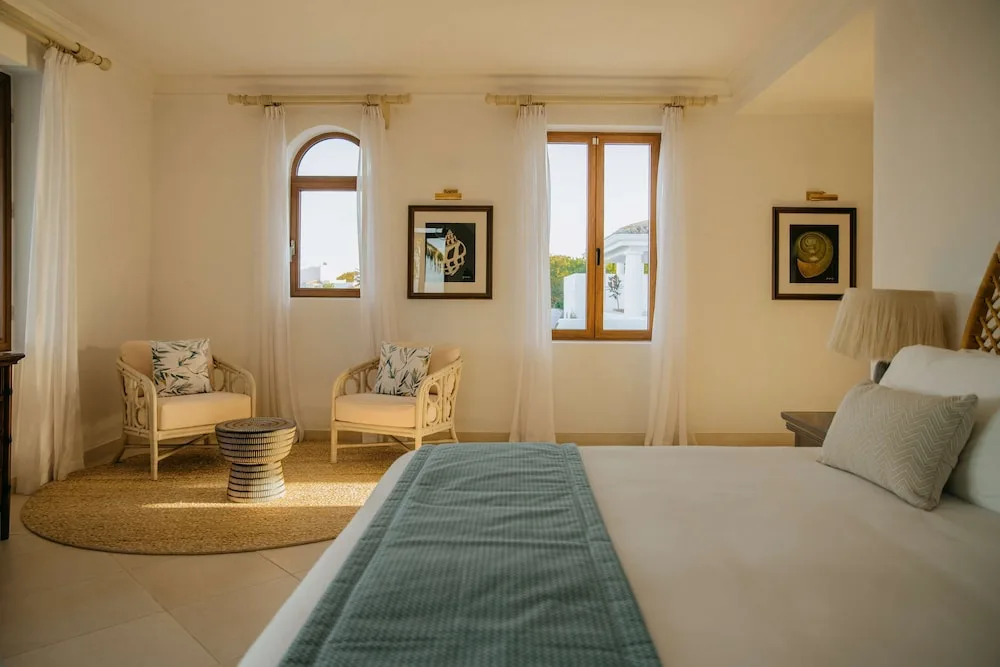 Guest room with bed, wicker chairs and arched window at La Samanna, St Martin.