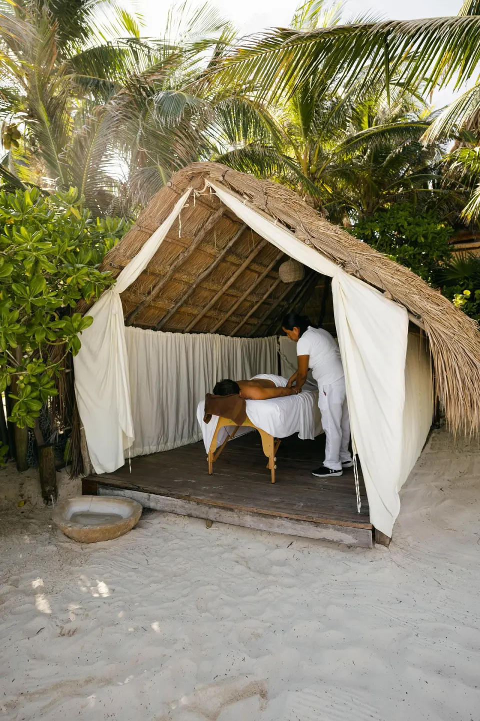 Therapist massaging a guest inside a small thatched beach cabana on sand at La Valise Tulum