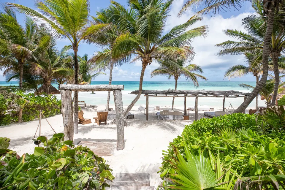 Beach pergolas and loungers with palm trees and ocean at La Valise Tulum
