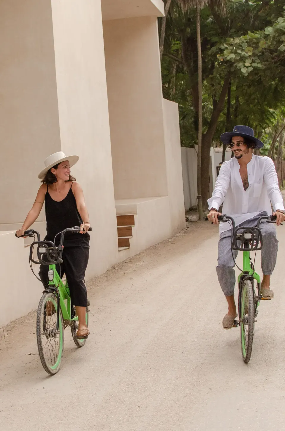 Two guests riding green bicycles along a sandy road at La Valise Tulum.