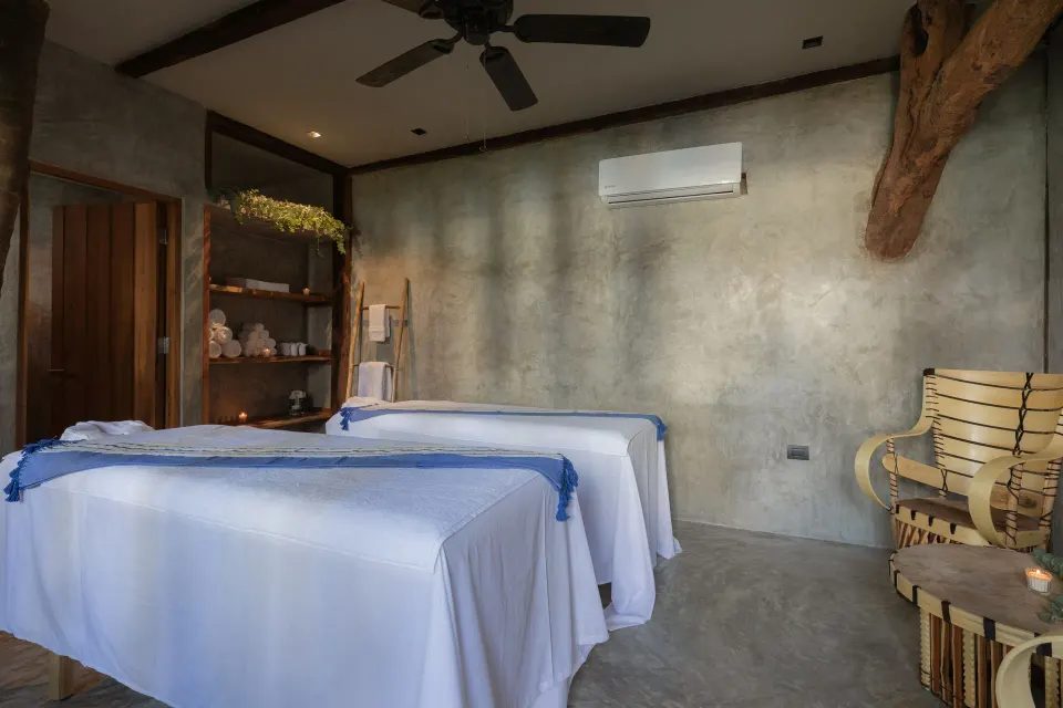 Spa treatment room with two massage tables and a fan at La Valise Tulum